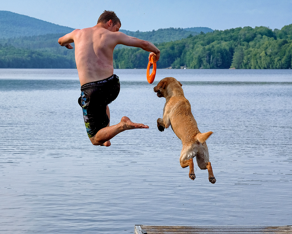 nh-lakes-jumping-in-with-dog Man jumping off a dock into a New Hampshire lake with his dog