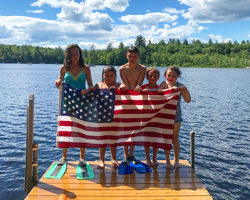 nh-lakes-kids-on-dock A group of kids standing on a dock with an American flag