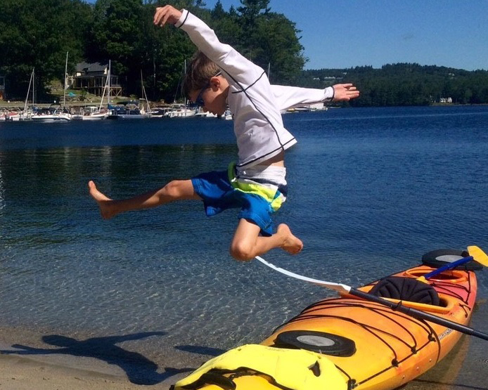 Young boy jumping in front of a New Hampshire lake